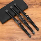 Infinity Leather Bracelet For Men - Black leather wristbands with braided and smooth sections, featuring gold and silver metal accents including infinity symbols and rectangular bars, displayed on a wooden surface next to a black leather pouch.