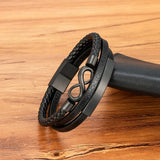 Infinity Leather Bracelet For Men - Black multi-strand leather bracelet with braided, smooth, and textured bands, featuring a matte black infinity symbol clasp and a rectangular slide clasp, displayed on a wooden surface.