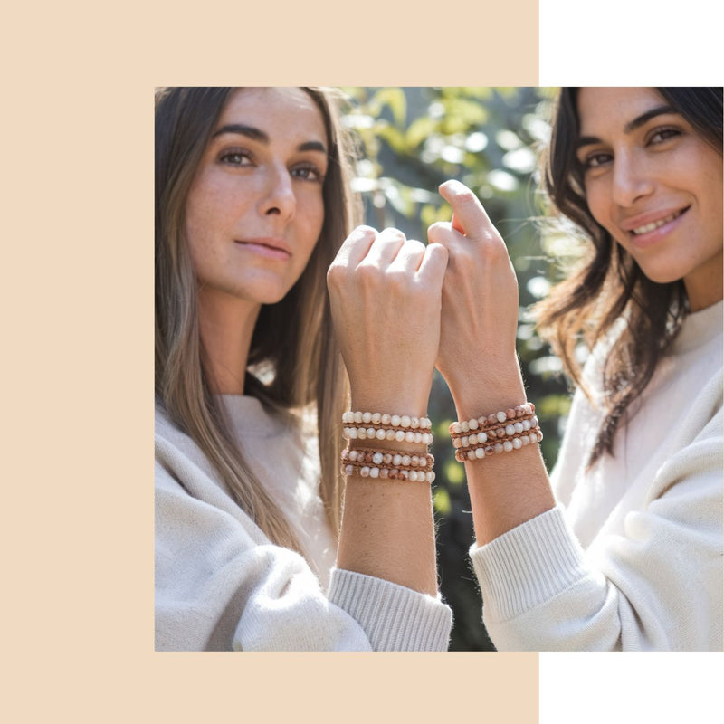 Two women wearing pearl bracelets outdoors with a beige background